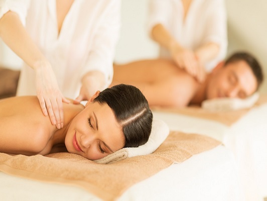 people, body care and relax concept - happy couple in spa salon lying on desks and having massage